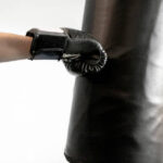 Box training, man's arm with black leather boxing glove punch direct to sandbag at the gym. Indoor sports activity for strength and physical health, isolated. Concept of fighter, challenge, professional